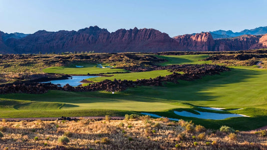 Expansive golf course with lakes, mountains, and a clear blue sky.
