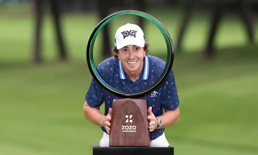 Golfer celebrating victory with a Zozo Championship trophy, green course in the background.