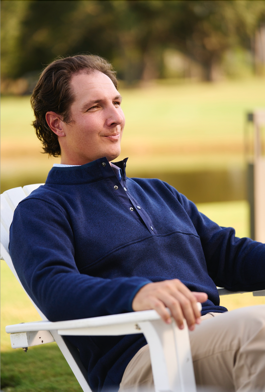 Golfer in a blue jacket, relaxed in a chair overlooking a green landscape.