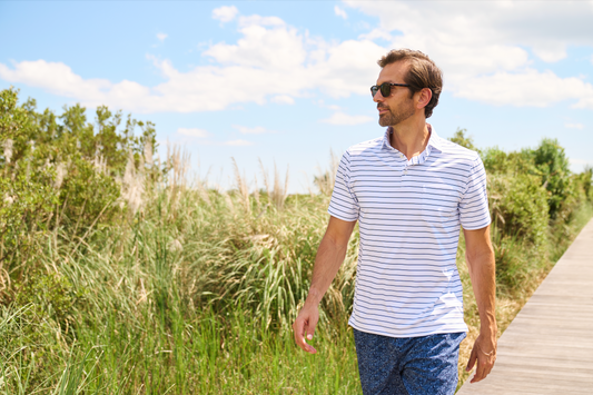 Man in sunglasses, walking on a wooden bridge overlooking a green field.