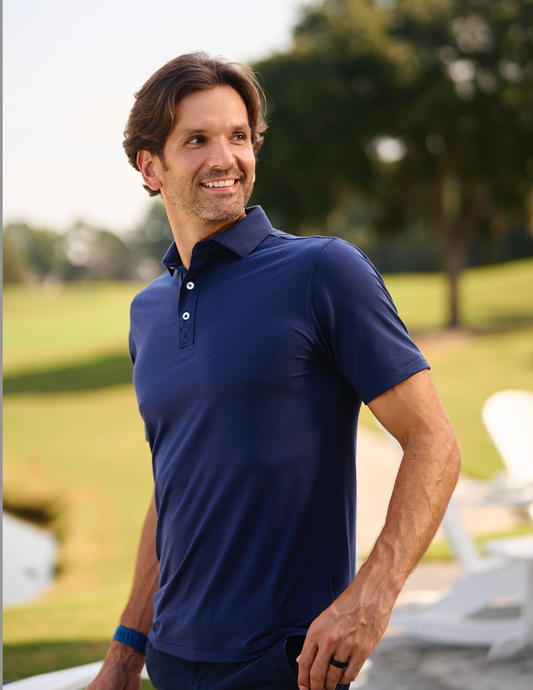 Man smiling wearing a polo blue t-shirt, blurred golf course in sunny day in the background.