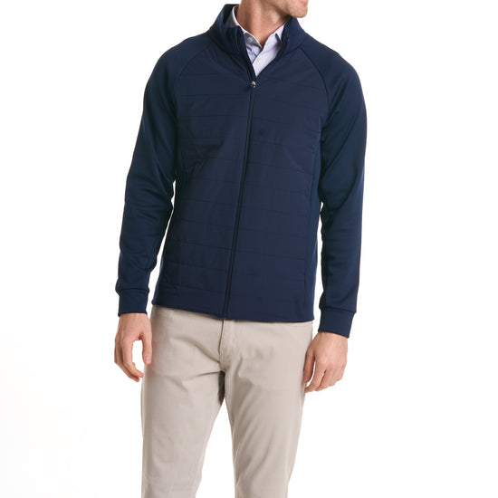 Close-up of a man wearingThe Traveler Jacket in Beaufain Blue with white pants, cropped from chin to knees, against a solid white background.