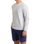 Close-up of a man wearing The Surfside Longsleeve Tee in Gaillard Gray with cream white color pants, cropped from chin to knees, against a solid white background.